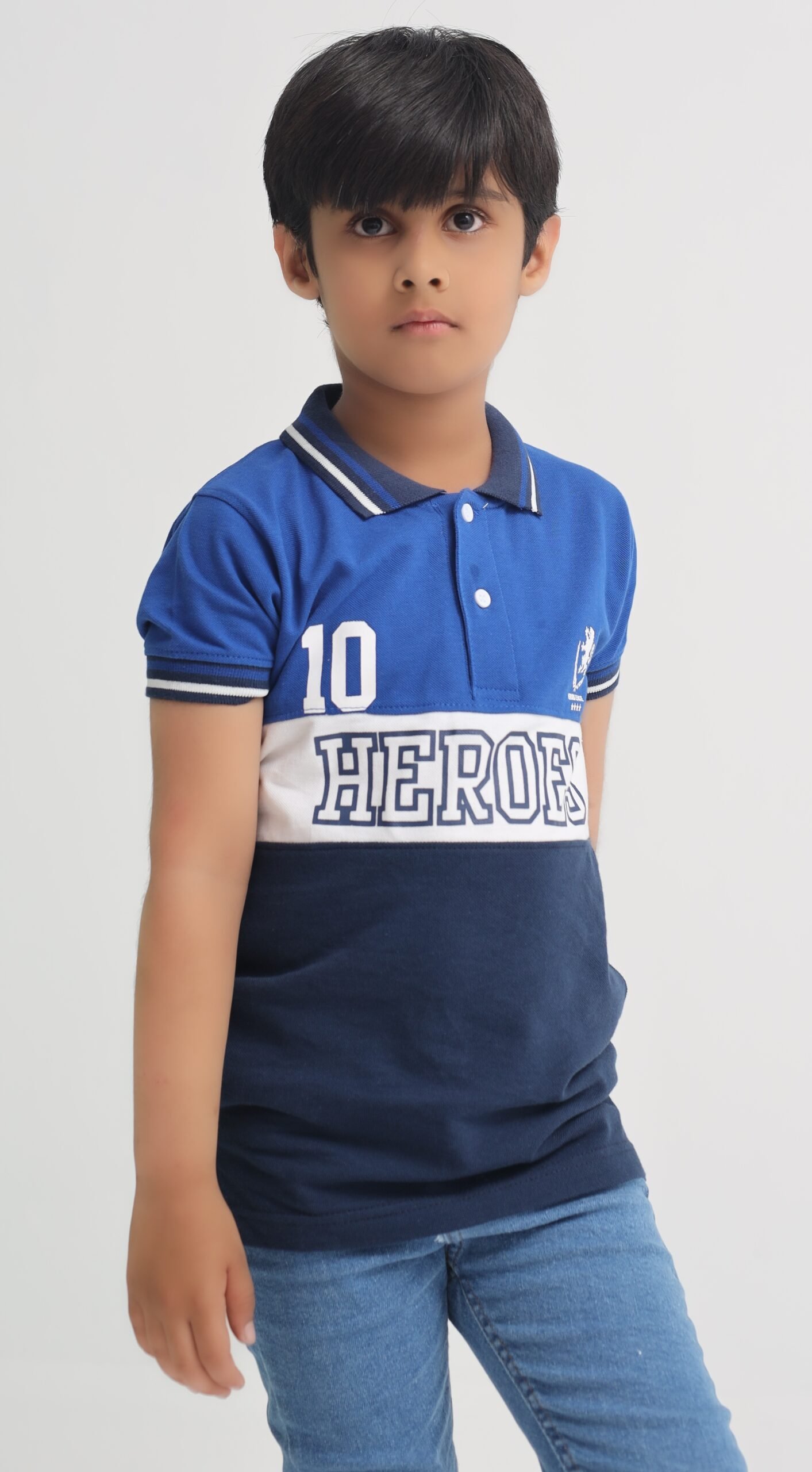 Boy wearing a royal blue, navy and white Heroes League cotton polo shirt with jeans