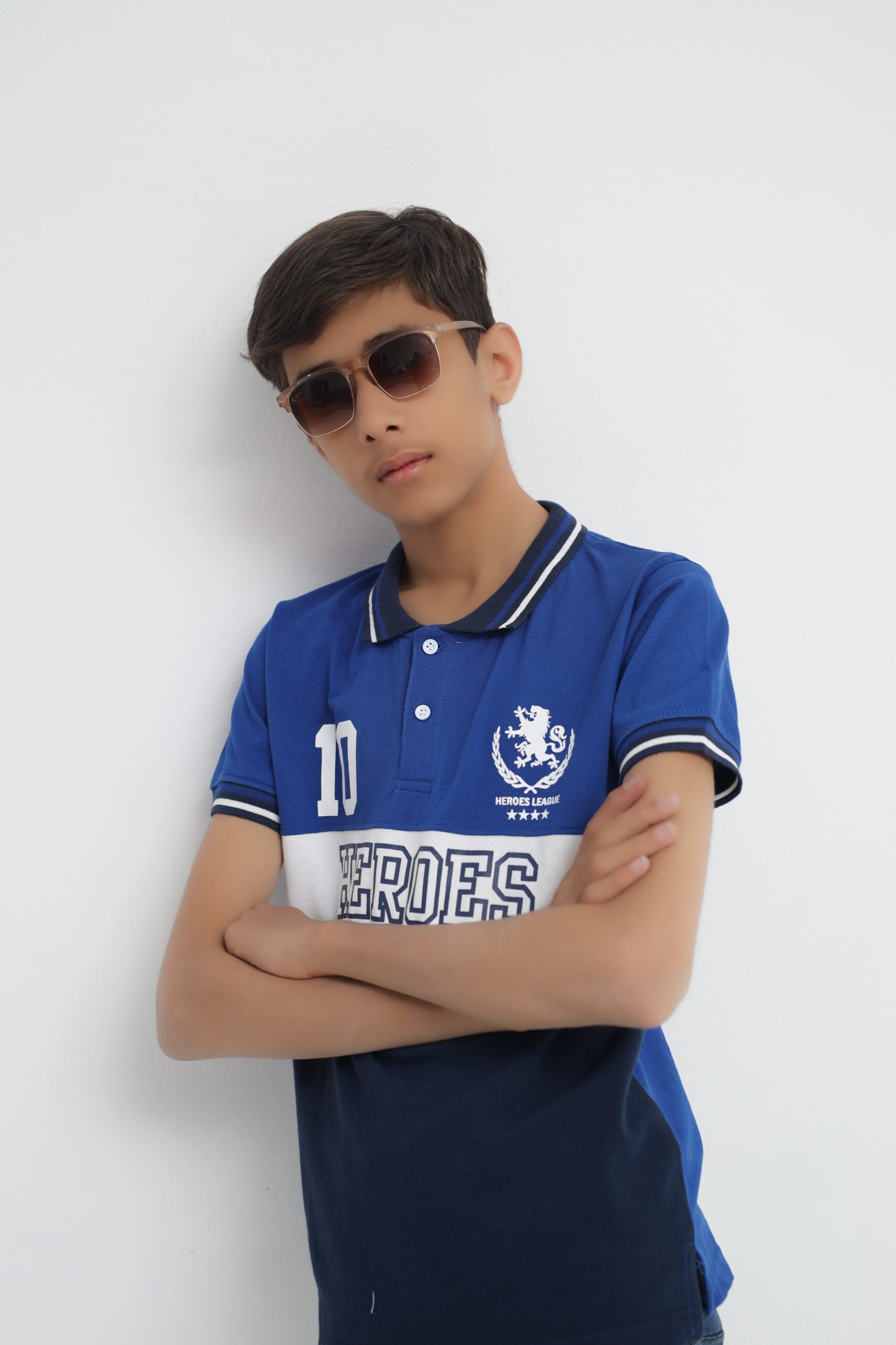 Boy wearing a blue Heroes League cotton polo shirt with sunglasses and folded arms