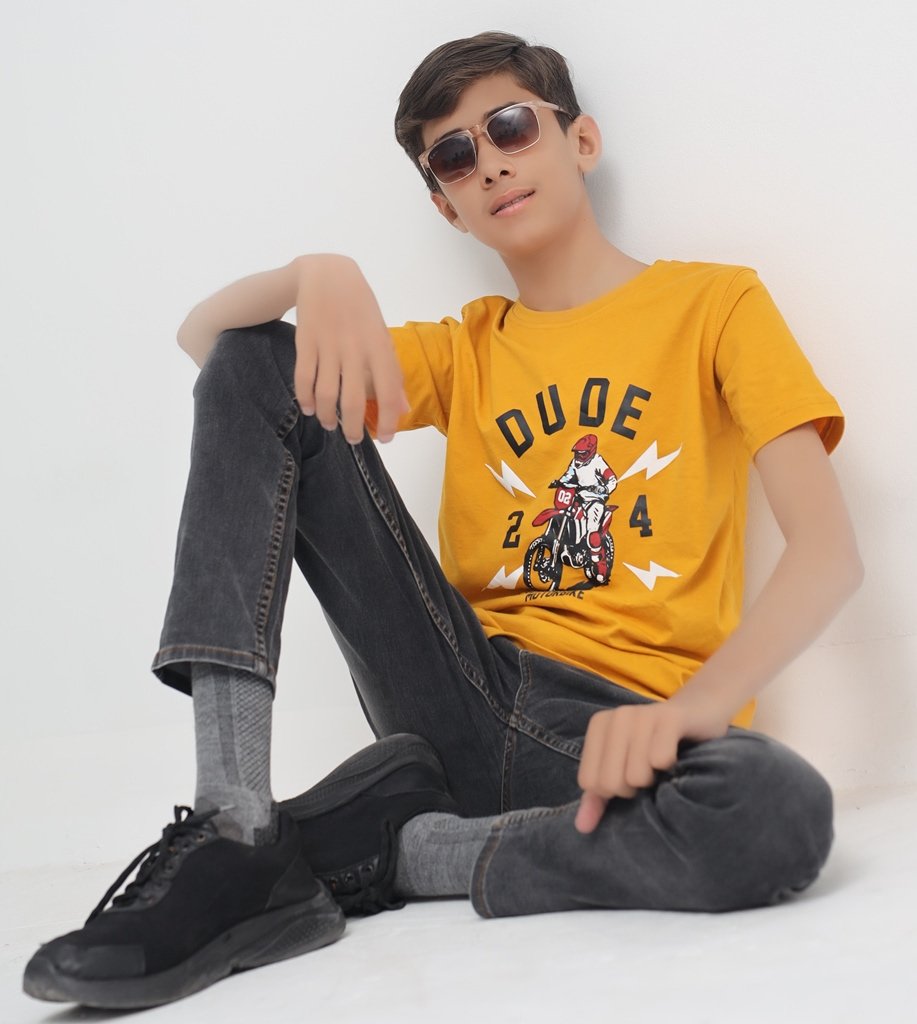 Boy wearing a mustard yellow motorcycle graphic T-shirt with black jeans